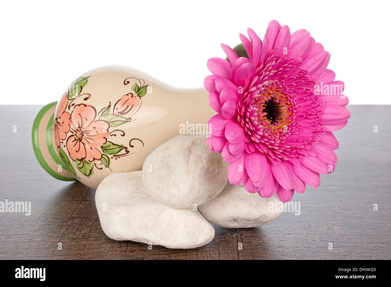 Pink Gerbera in decorated vase on a pile of white stones on a dark brown wooden shelf Stock Photo