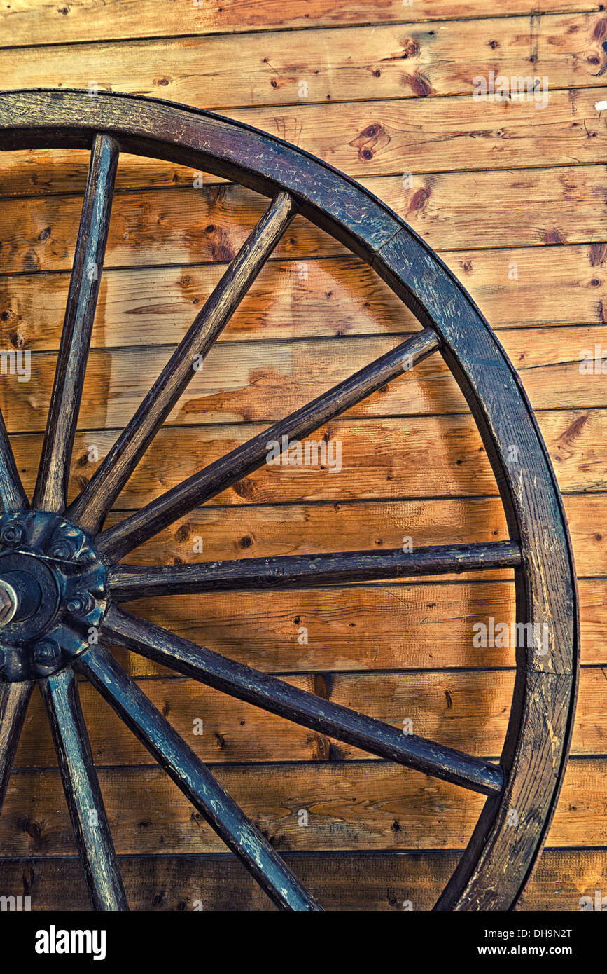 Old horse carriage wooden wheel leaning on the wooden wall Stock Photo