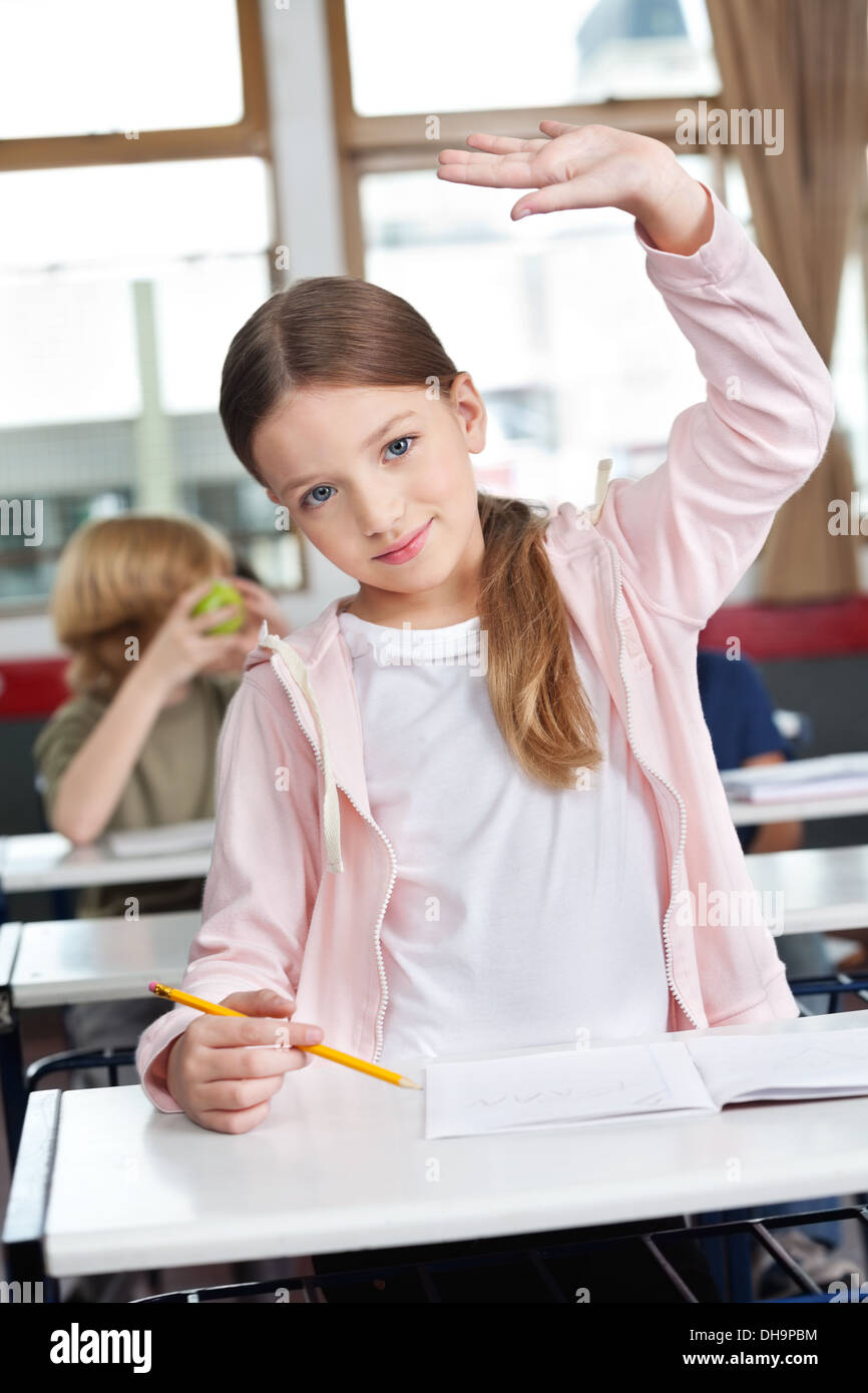 Schoolgirl Raising Hand At Desk In Classroom Stock Photo - Alamy