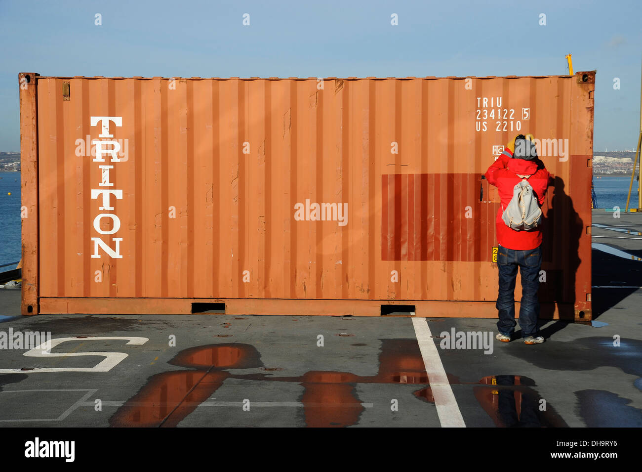 Man in a red Coat taking photographs of a red shipping container Stock Photo