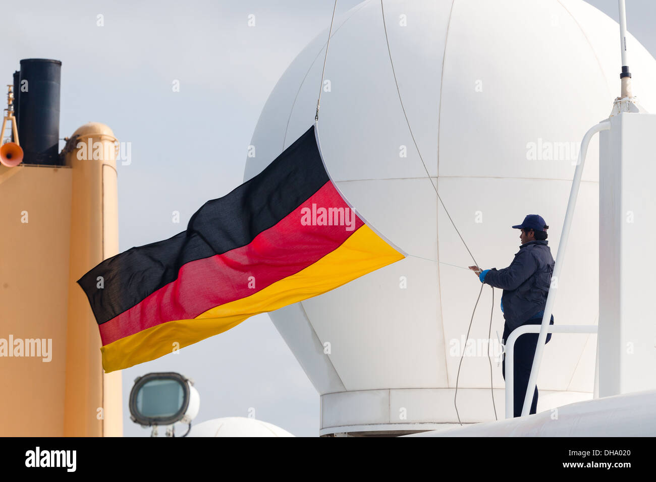 Crewman lowering German flag on departure from German port of Rostock. Stock Photo