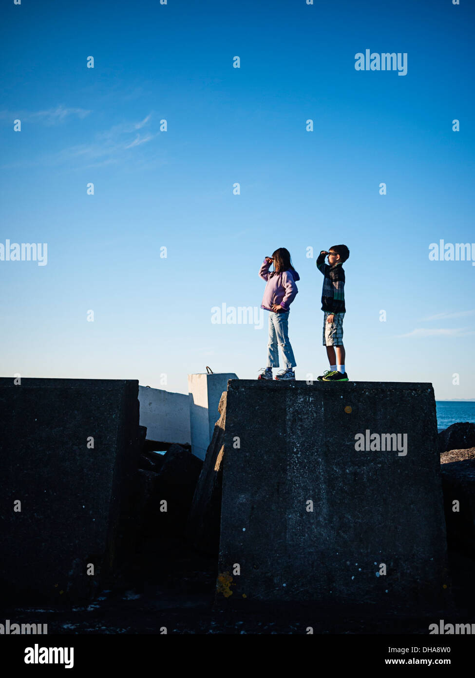 Boy and girl stand on harbour wall and look out to sea. Stock Photo