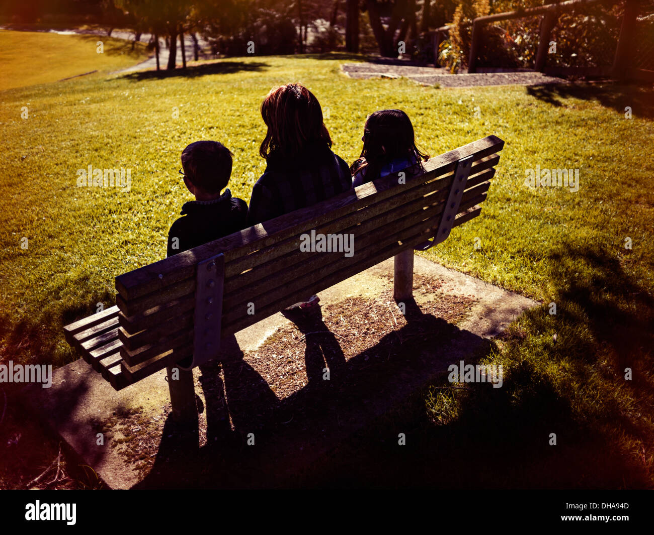 Mother, son and daughter sit on park bench on sunny winter day Stock Photo