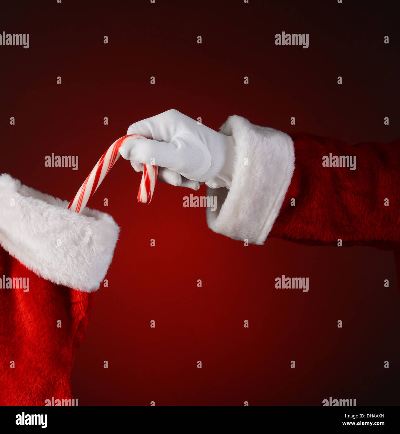 Closeup of Santa Claus placing a candy cane into a holiday stocking. Square format on a light to dark red spot background. Stock Photo