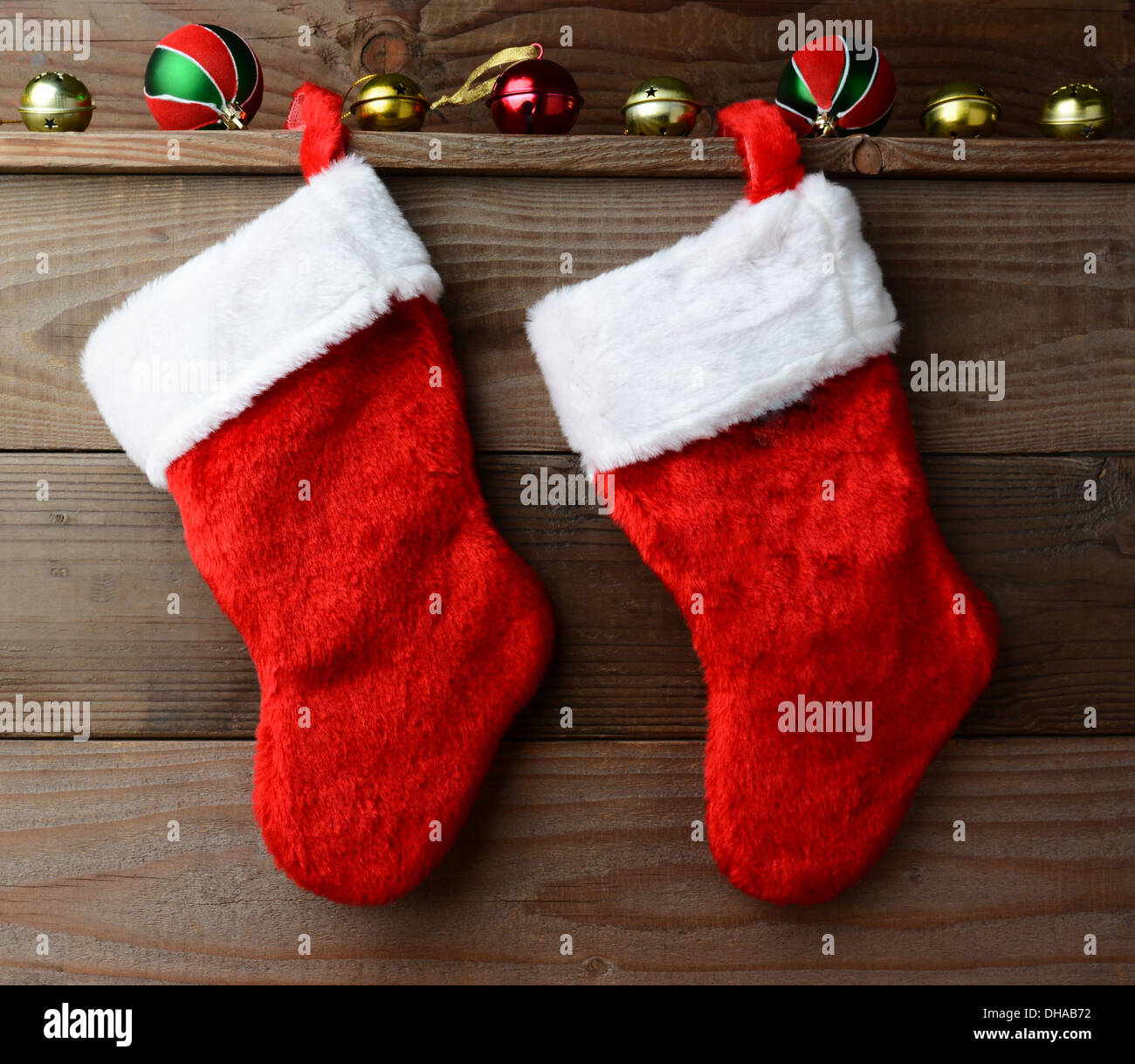 Two Christmas stockings hung on a rustic wooden wall with sliegh bells and ornaments. Stock Photo