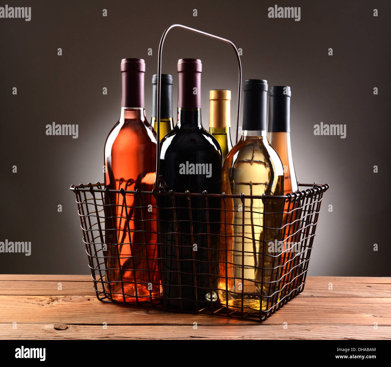 A wire shopping basket filled with assorted wine bottles. The basket is sitting on a rustic wooden table Stock Photo