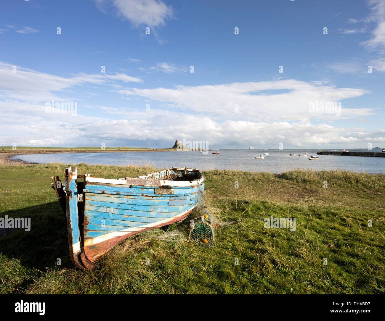 Old wooden Coble fishing boats on Holy Island and the distant Lindisfarne Castle, Northumberland, England, UK Stock Photo