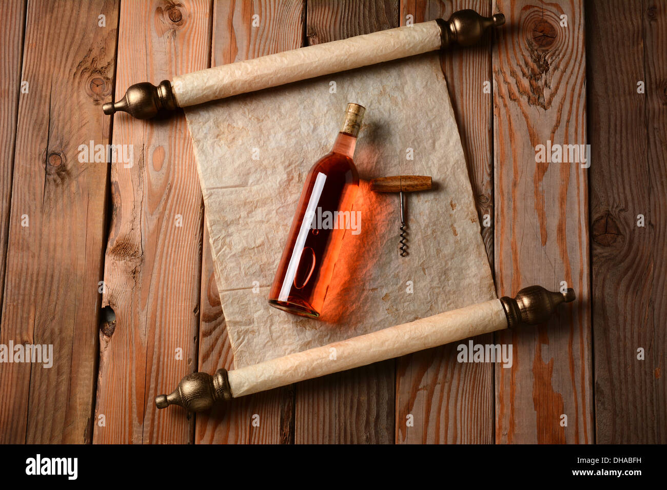 A bottle of blush wine and corkscrew laying on a scroll of parchment paper on a rustic wooden floor. Stock Photo