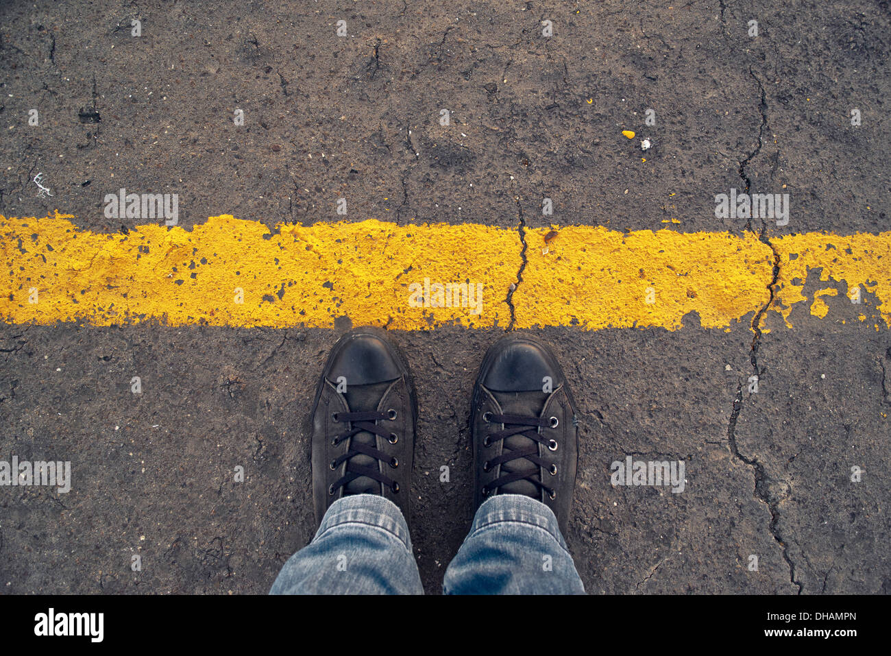 Male sneakers on the asphalt road with yellow line. Border line concept, danger or warning sign. Stock Photo