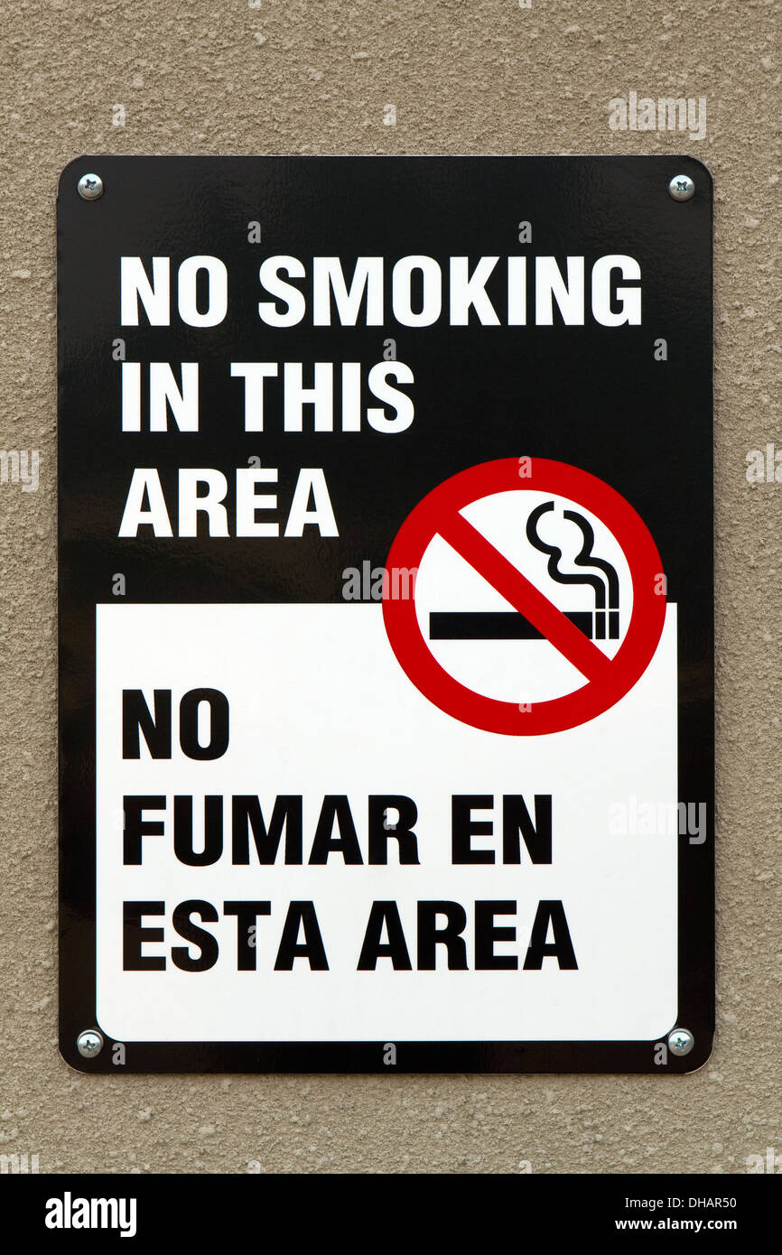 Bilingual no smoking sign with graphic and written in the English and Spanish languages is screwed to a wall. Stock Photo