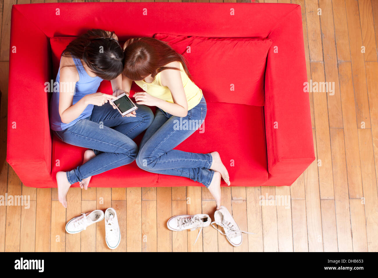 Two female friends playing with cellular telephone on red sofa,smiling Stock Photo