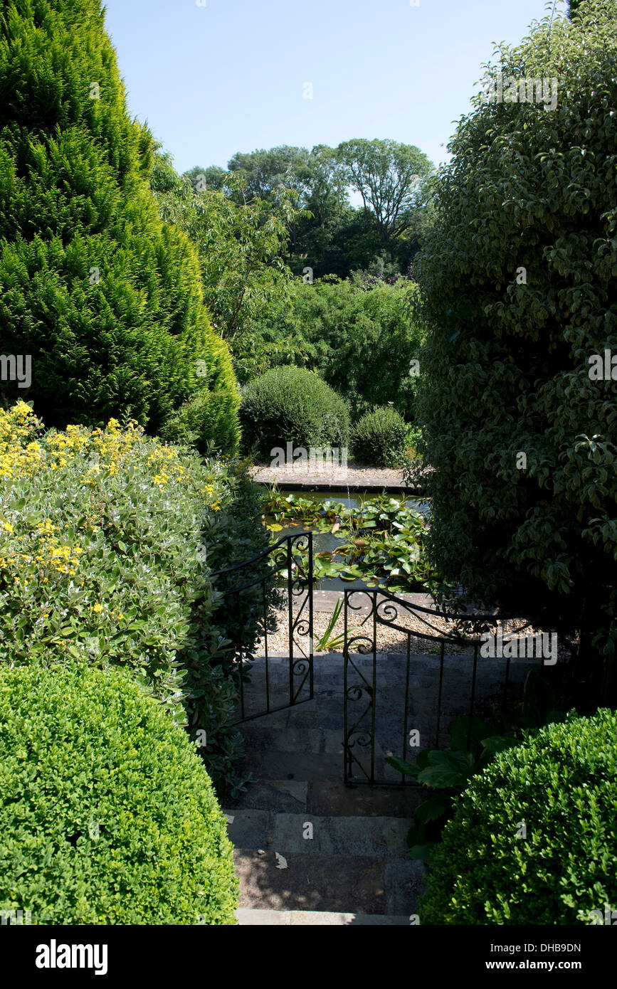 Garden steps through shrubs leading down through a gate to a pond Stock Photo