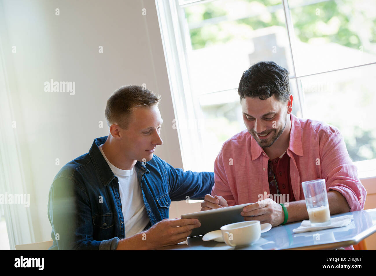 Two men at a cafe table, using a digital tablet. Stock Photo