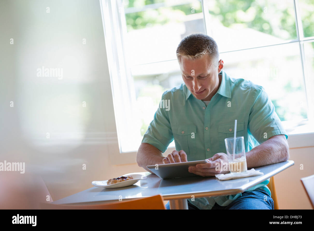 A man with short cropped hair sitting at a cafe table. Using a digital tablet. Stock Photo