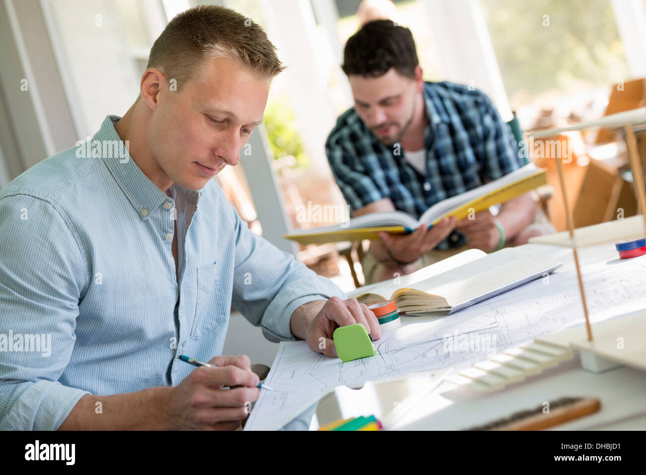 Two men seated at a table using books and a digital tablet. Stock Photo