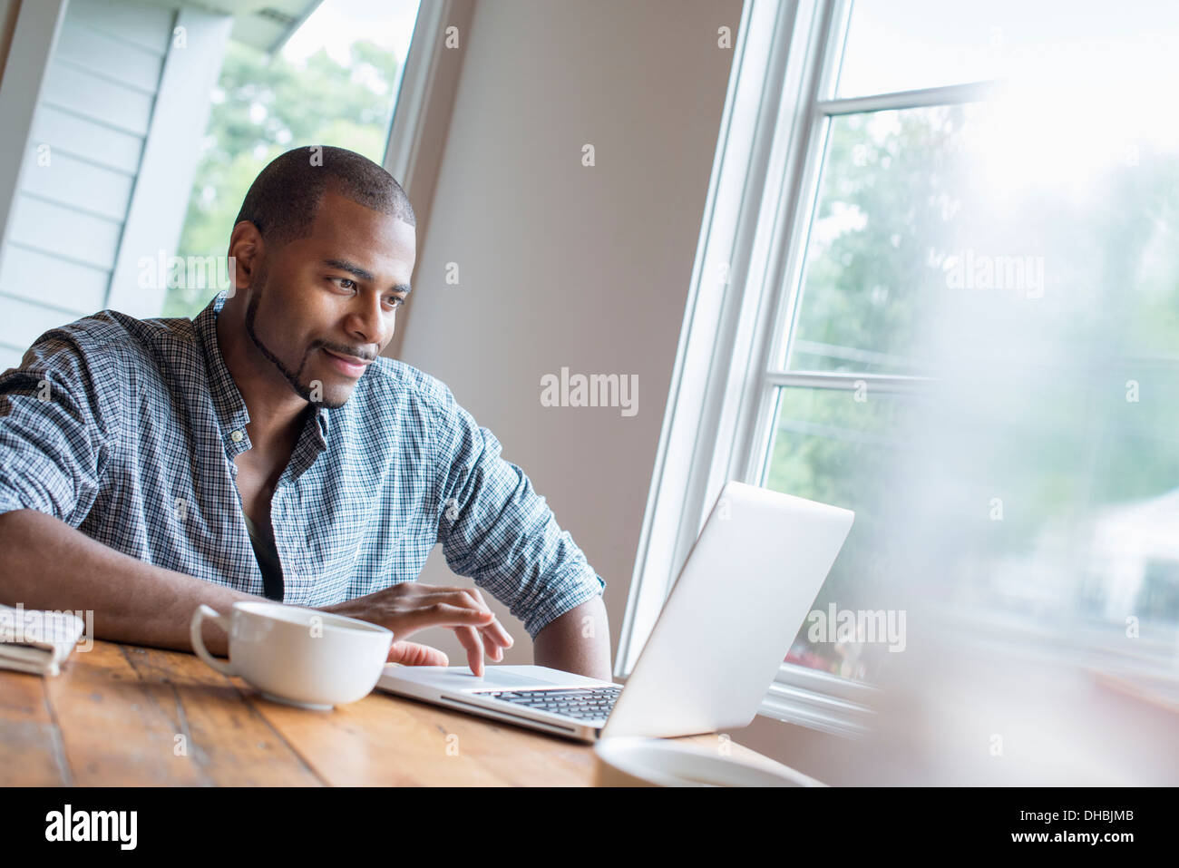 A man sitting in a cafe with a cup of coffee, using a laptop computer. Stock Photo