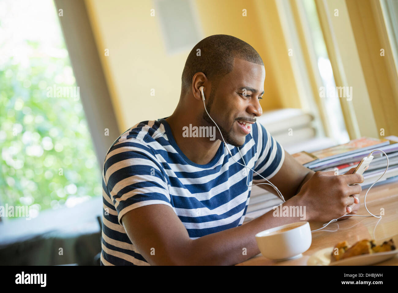 A man sitting in a cafe, having a cup of coffee, listening to music with headphones. Stock Photo