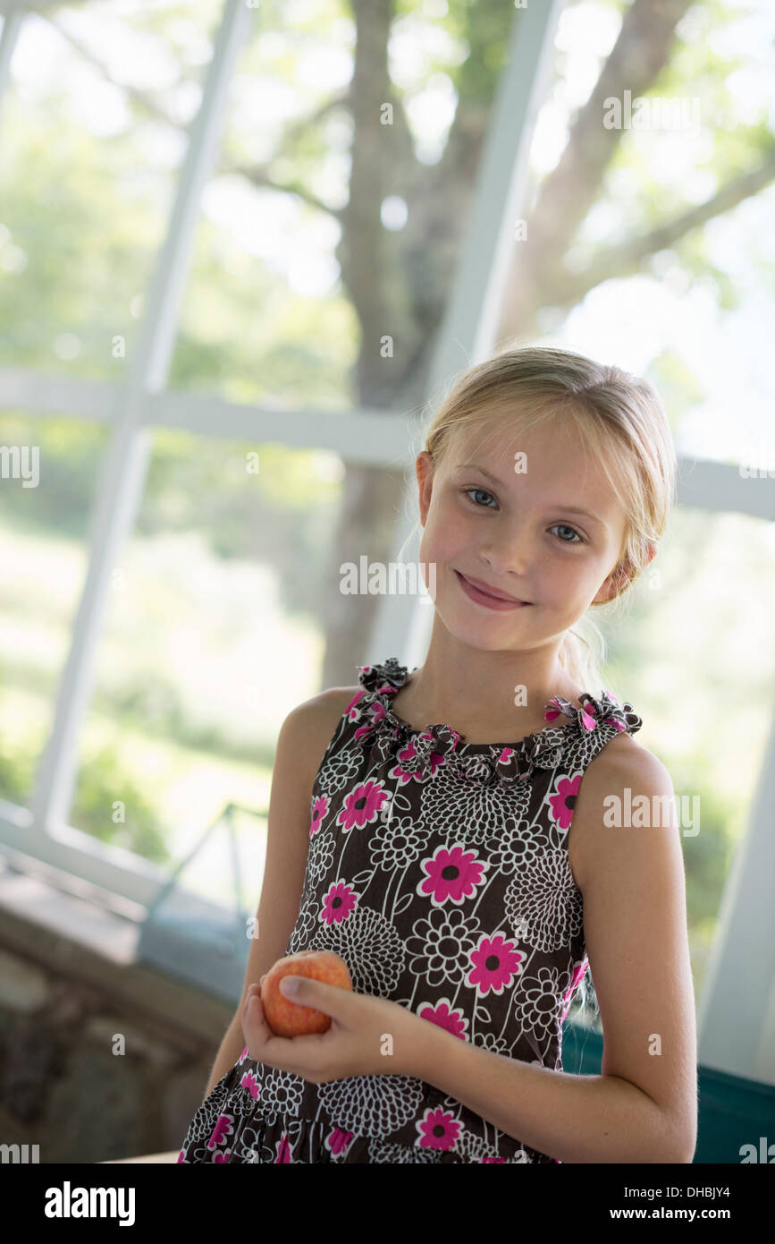A young girl in a floral dress holding a peach fruit. Stock Photo