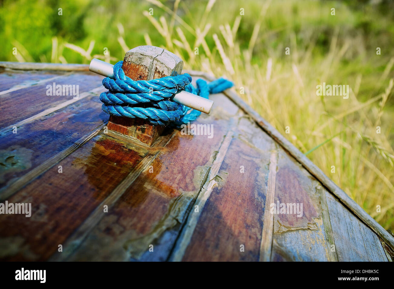 Abstract image of bow (front) of small wooden boat with blue rope coiled around a short post with grass in the background. Stock Photo
