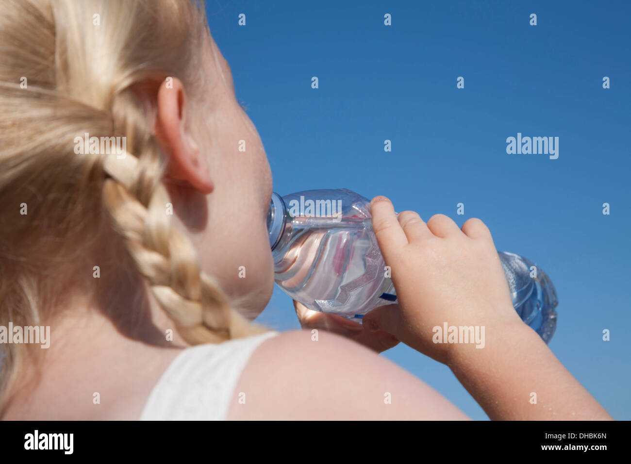 A young child with blonde hair in pigtails, drinking water from a clear bottle. Stock Photo