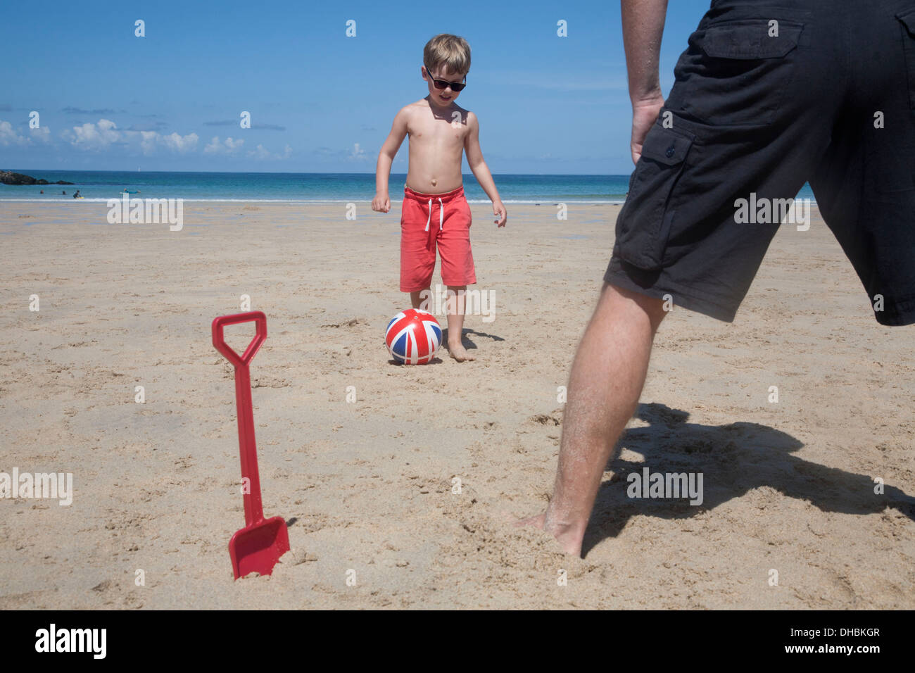 A boy playing football with a man on the sand. Father and son. A beach spade upright in the sand. Stock Photo