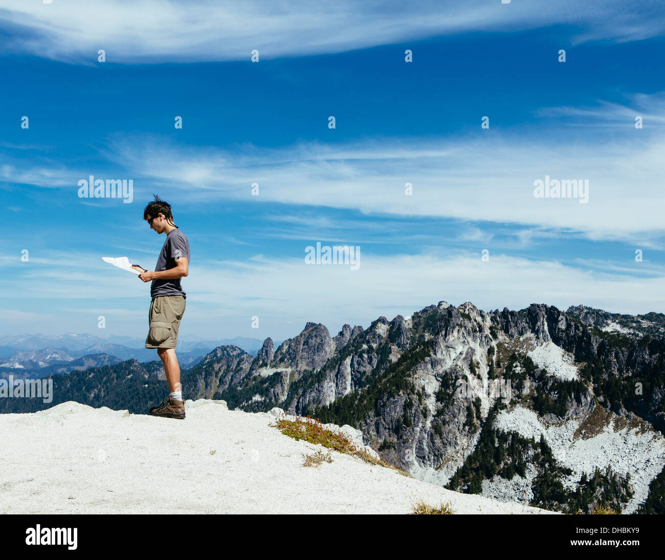 A hiker on mountain summit looking at map. Surprise Mountain Alpine Lakes Wilderness in Mount Baker-Snoqualmie National Forest, Stock Photo