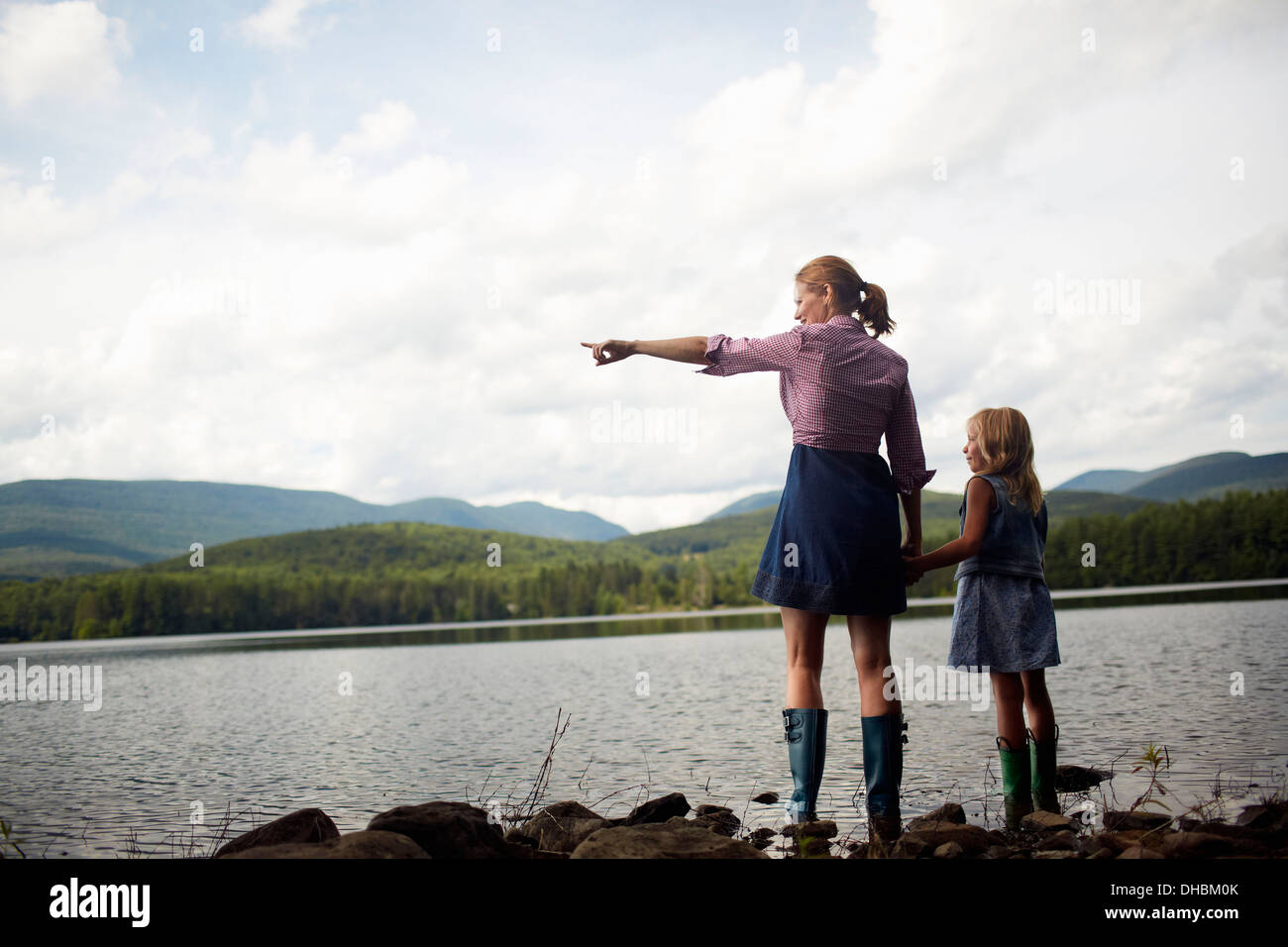 Two people, a woman and a child standing side by side and looking over water. Stock Photo