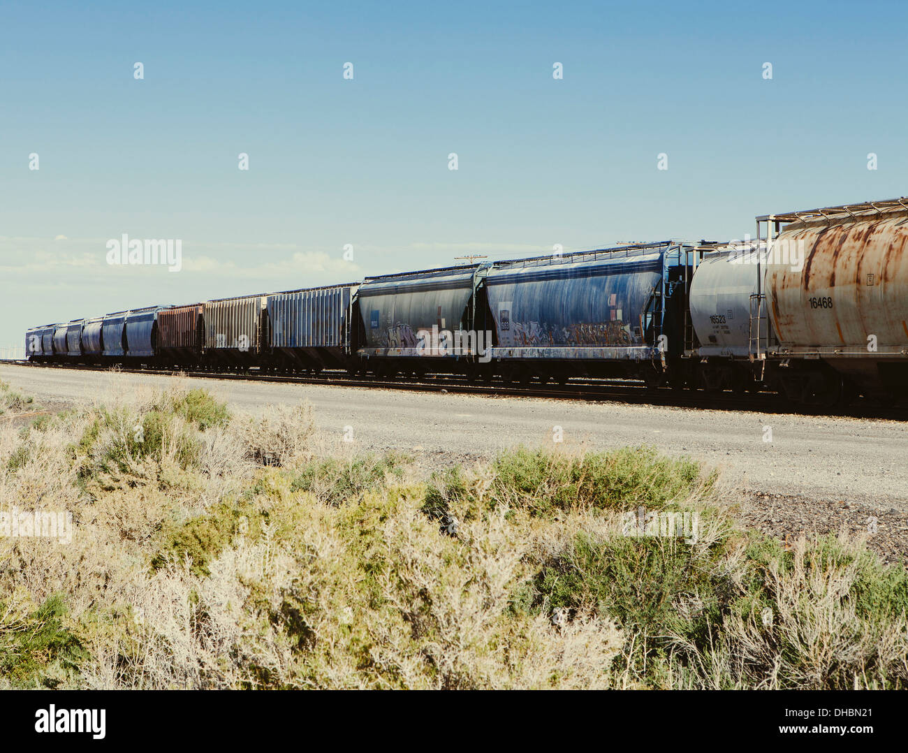 Row of container freight wagons of a freight train crossing the plains near Wendover. Scrubby sage bushes growing by the track. Stock Photo