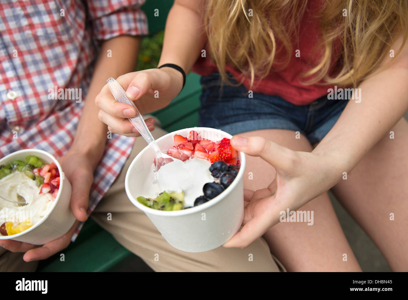 Young people sitting side by side, eating fresh organic fruit and yoghurt desert. Stock Photo