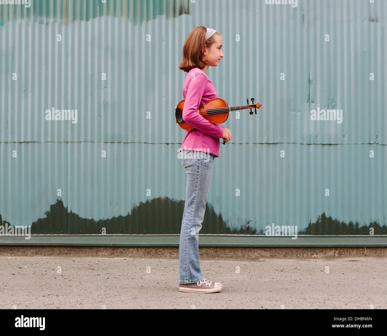 A ten year old girl holding a violin under her arm, standing on a street. Stock Photo