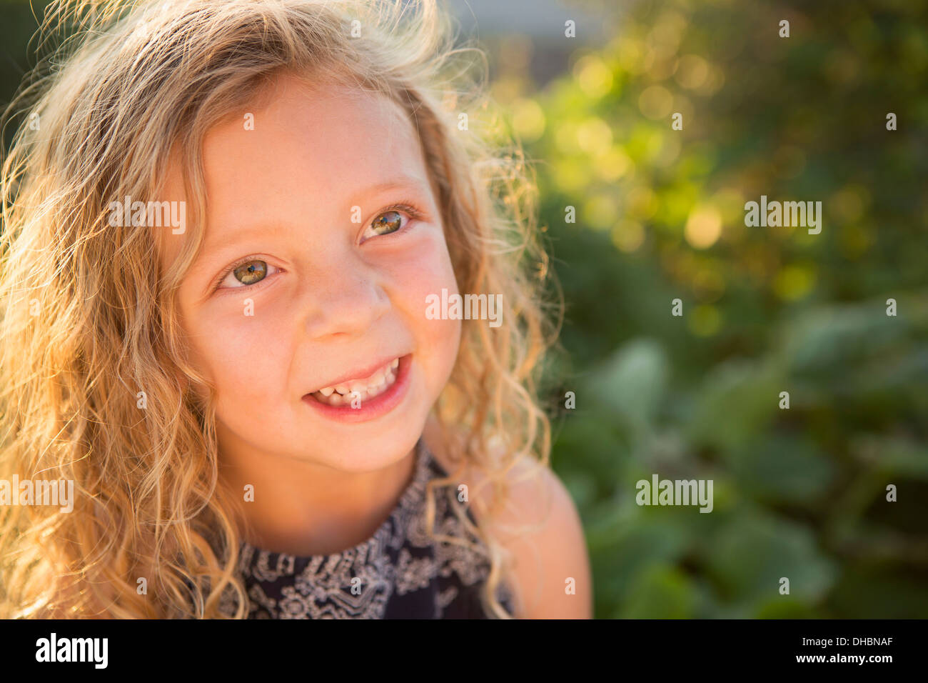 A young girl with long red curly hair outdoors in a garden. Stock Photo