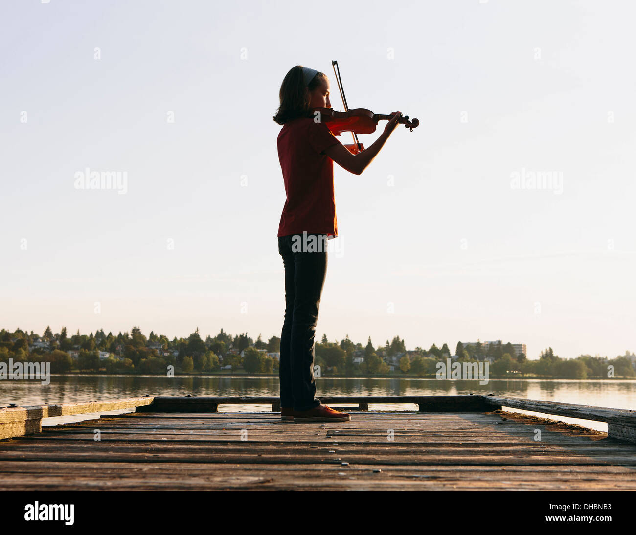A ten year old girl playing the violin at dawn on a wooden dock. Stock Photo