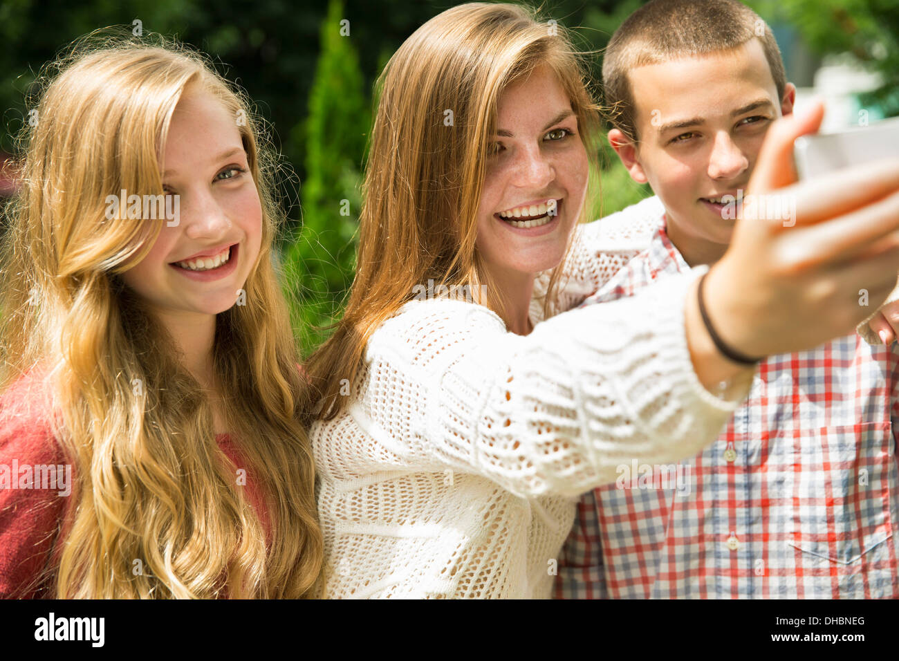 Three young people, two girls and a boy, posing and taking selfy photographs. Stock Photo