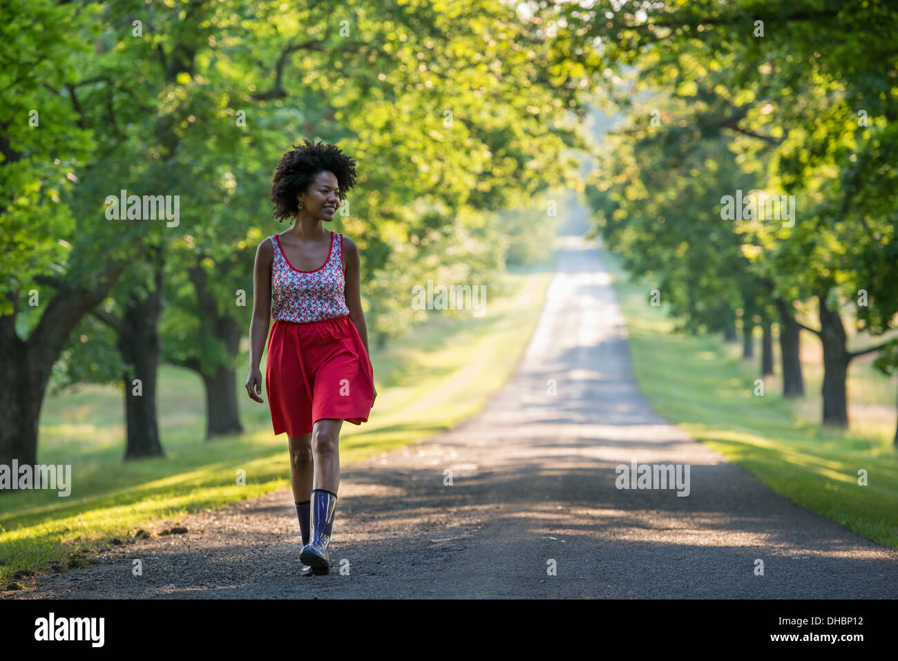 A woman walking down a tree lined path. Stock Photo