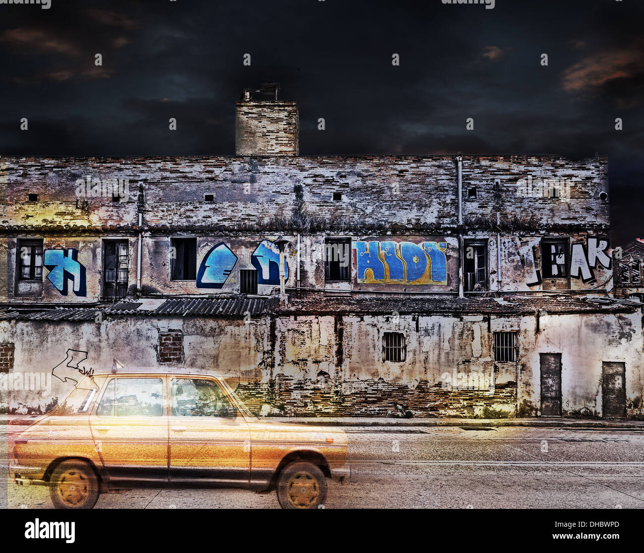 A yellow retro car driving past a derelict building with graffiti on it. The picture is color in a landscape format. Stock Photo