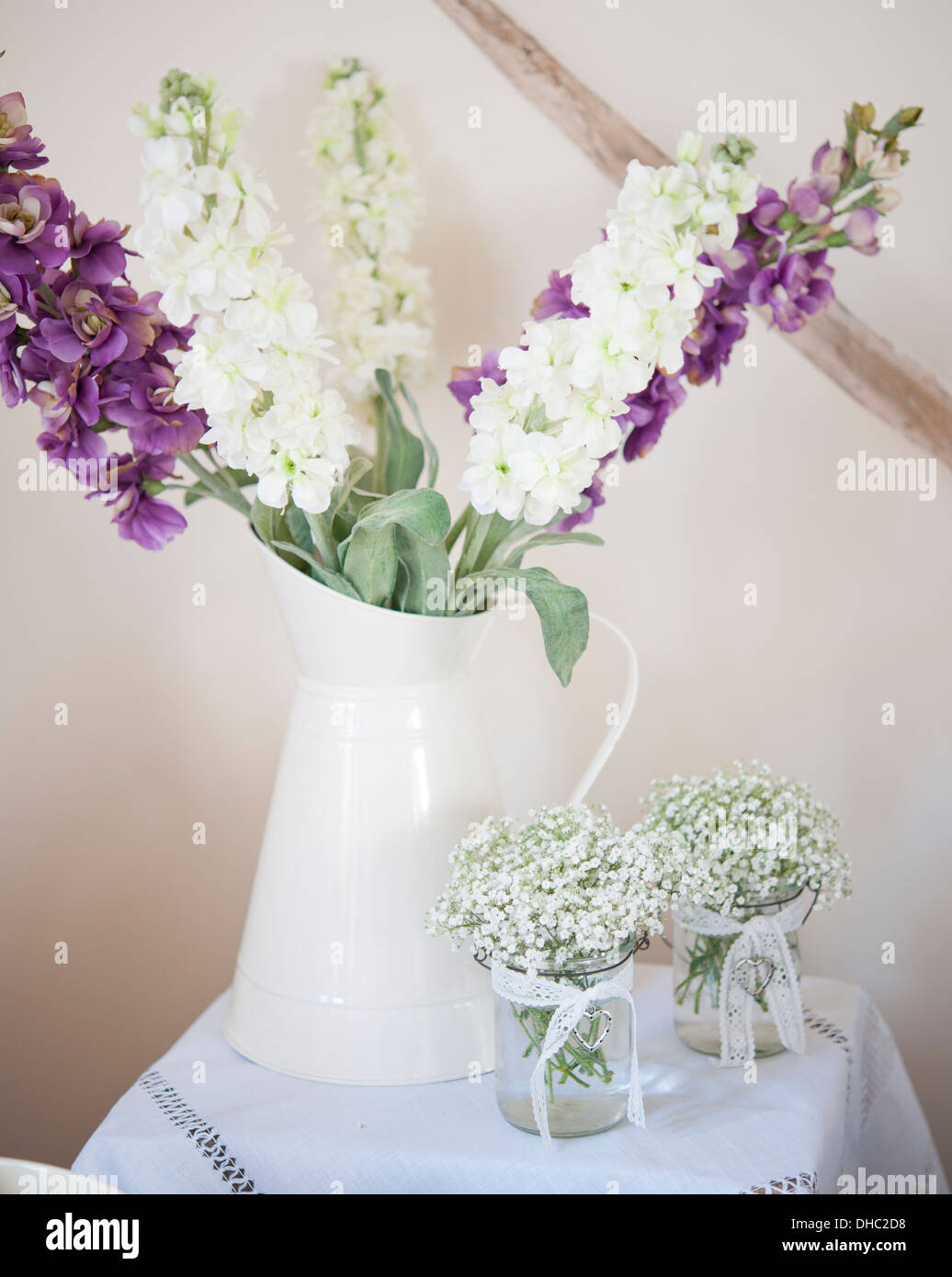 A Jug Of Purple And White Flowers With Two Small Vases Of White