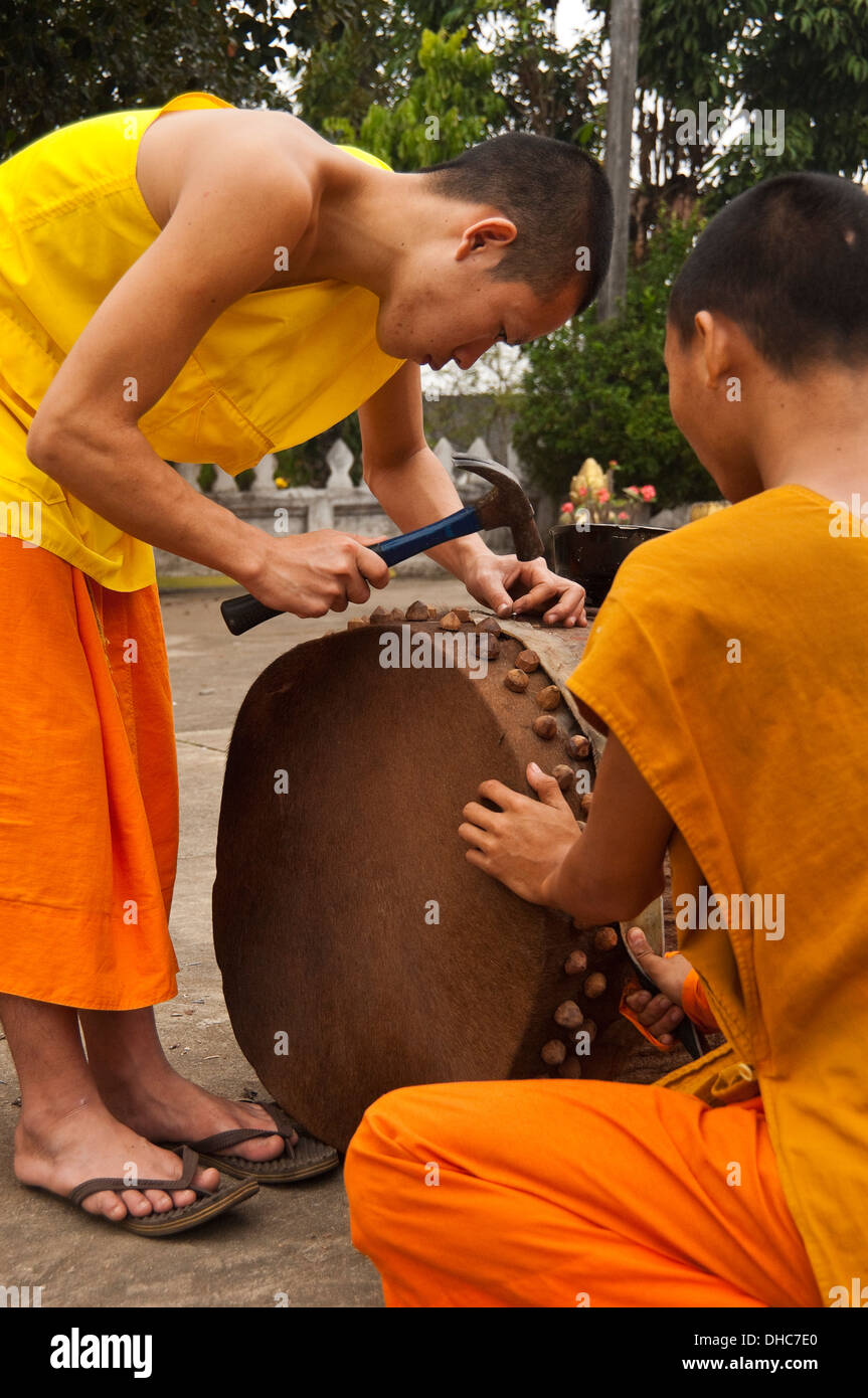 Vertical portrait of young Buddhist monks mending a ceremonial drum at their temple in Luang Prabang. Stock Photo