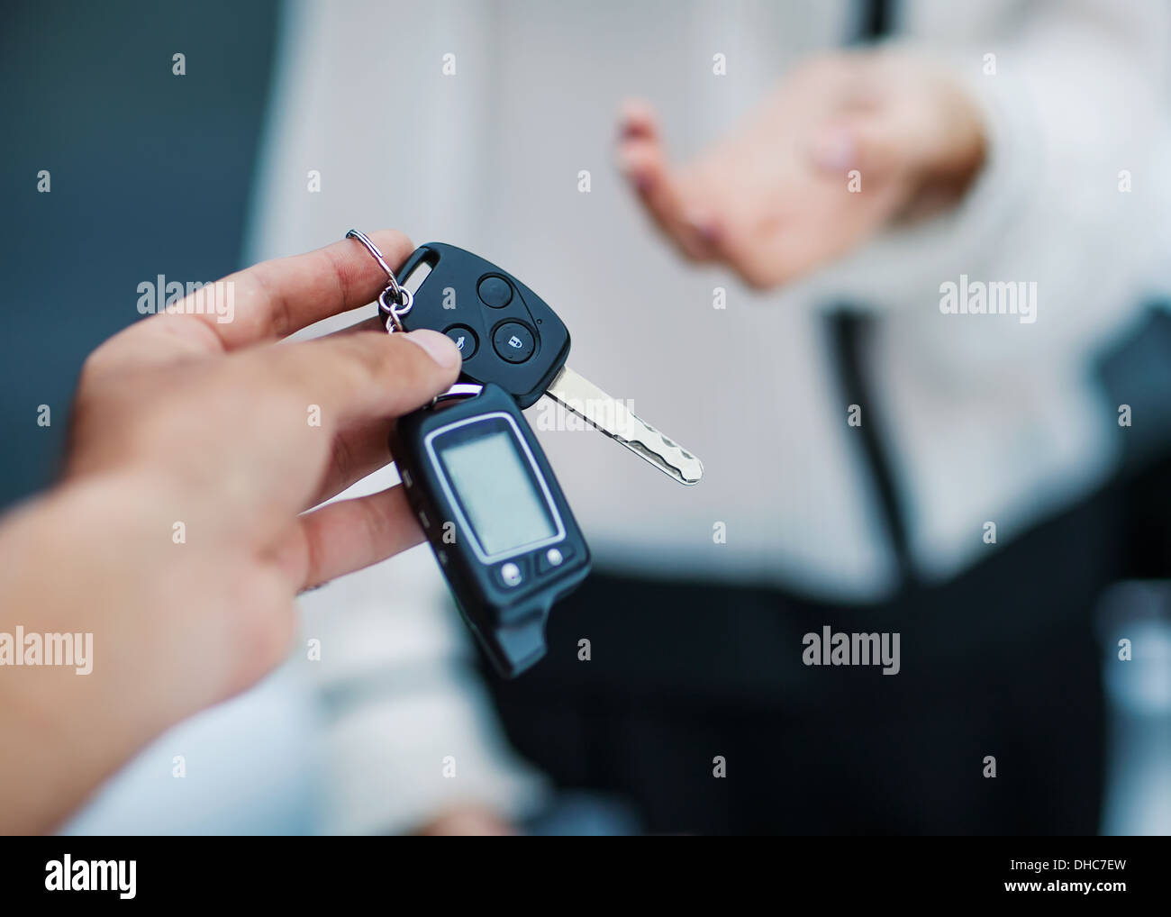 Male hand giving car key to female hand. She is holding a cell phone. In the background, a fragment of the car. Stock Photo