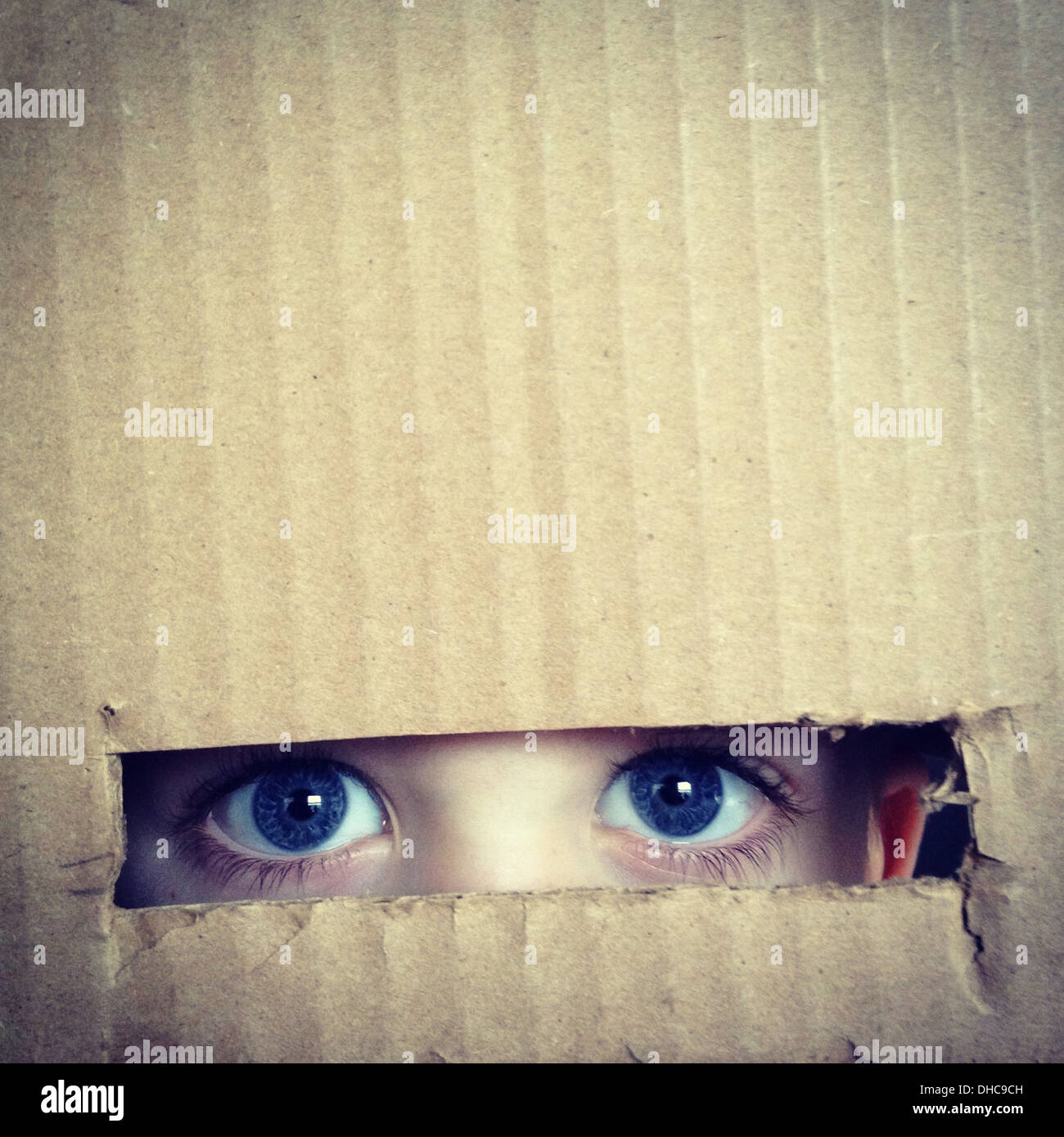 Boy's Eyes Looking Through Hole in Cardboard Box, Close Up Stock Photo