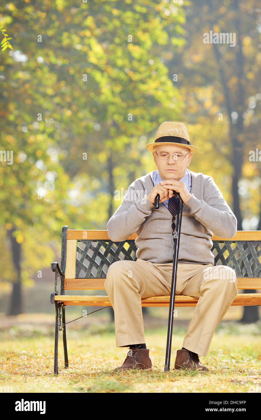 Thoughtful senior man with a cane sitting on a wooden