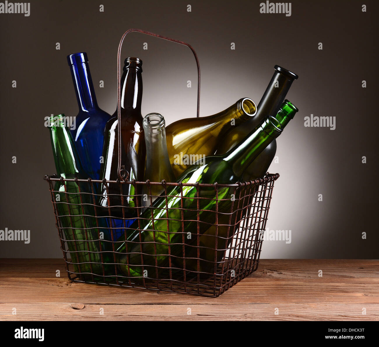 A wire shopping basket filled with assorted empty bottles. The basket is sitting on a rustic wooden table Stock Photo