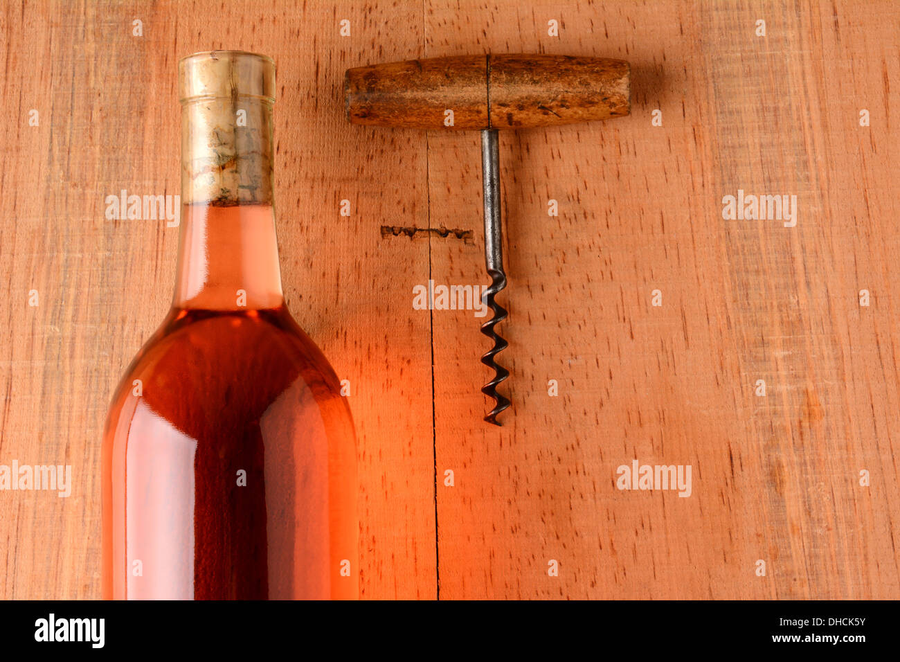 A blush wine bottle and corkscrew on a rustic wood surface with strong side light. Closeup in horizontal format with copy space. Stock Photo