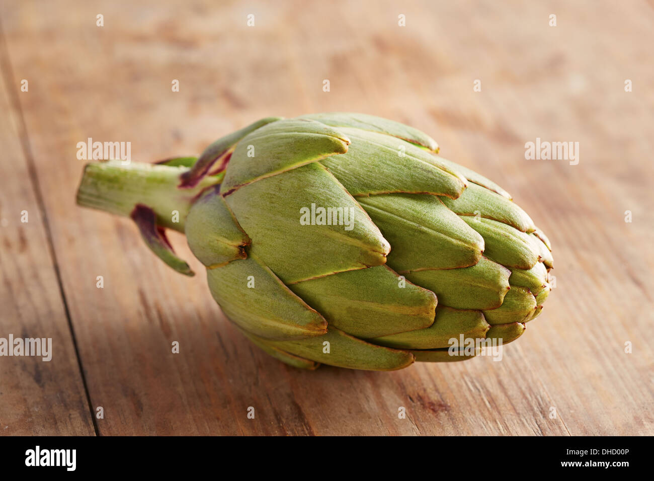 Single raw artichoke on wooden table Stock Photo