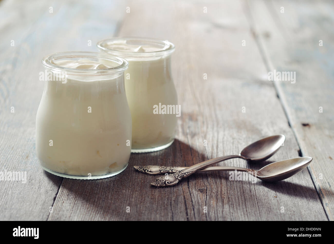Greek yogurt in a glass jars with spoons on wooden background Stock Photo