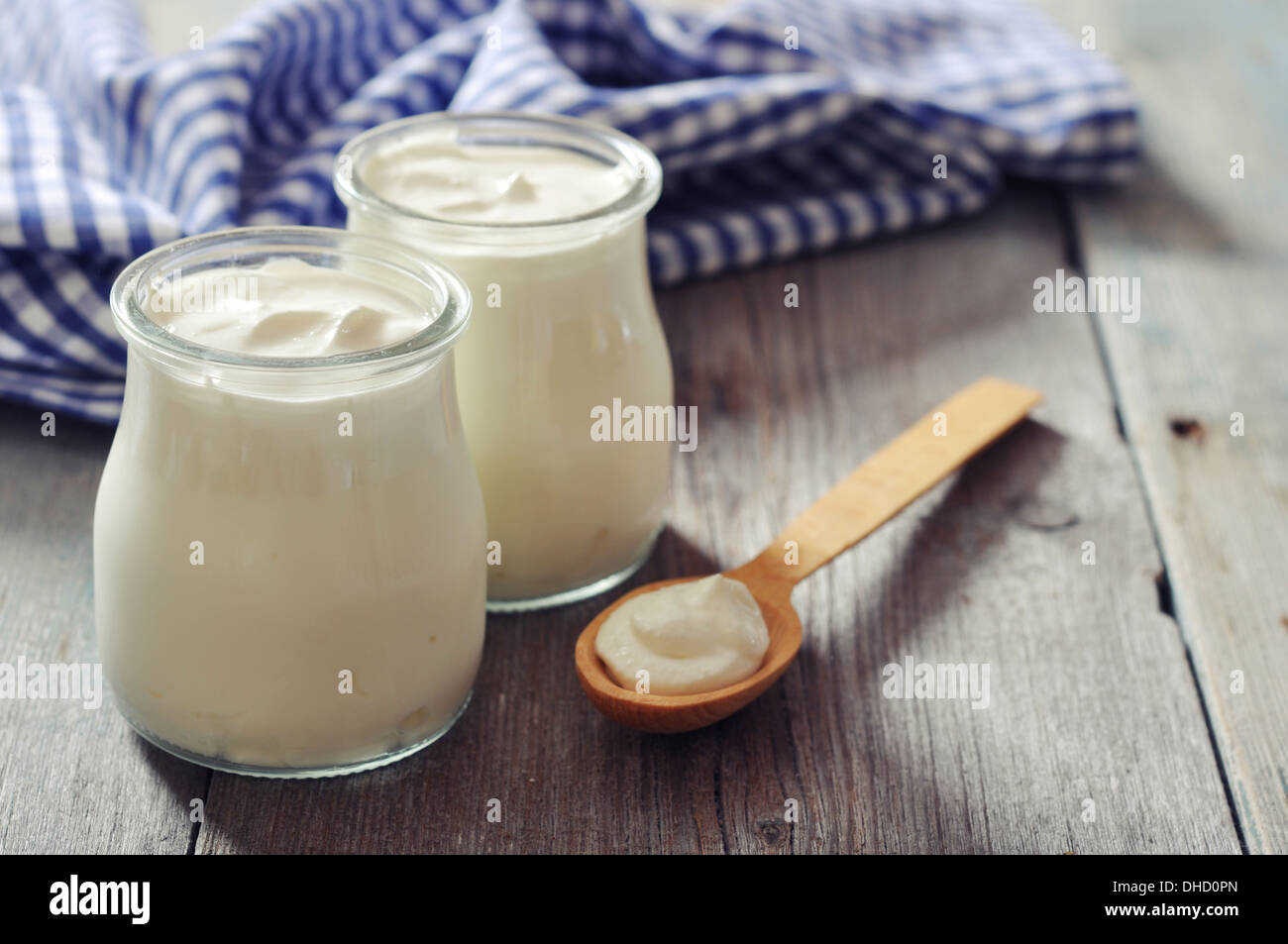 Greek yogurt in a glass jars with spoons on wooden background Stock Photo