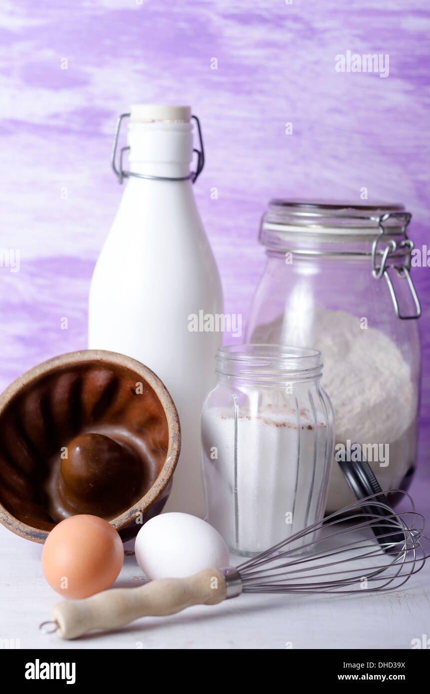 Cake pan, flour, eggs, milk, sugar and egg whip on table Stock Photo