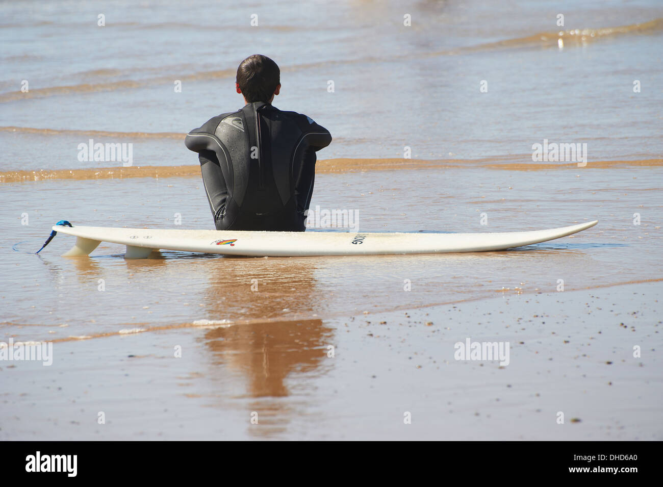Surfer sitting on the beach by his board Stock Photo