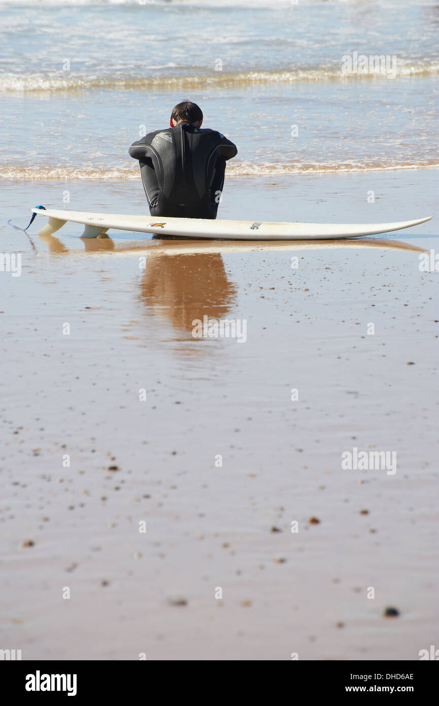 Surfer sitting on the beach by his board Stock Photo