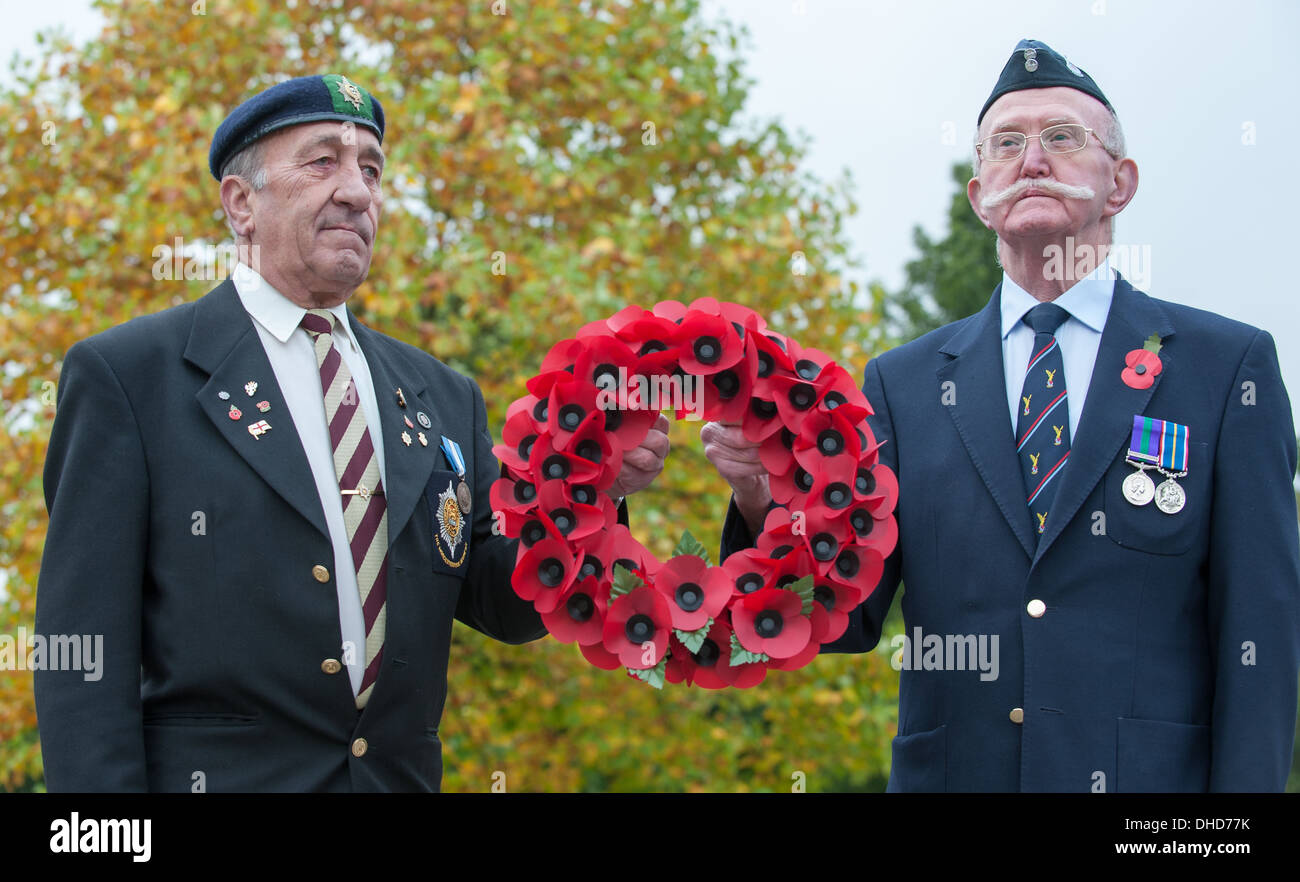 Two Second World War veterans stand to attention holding a wreath of Royal British Legion poppies by autumnal arboretum trees Stock Photo