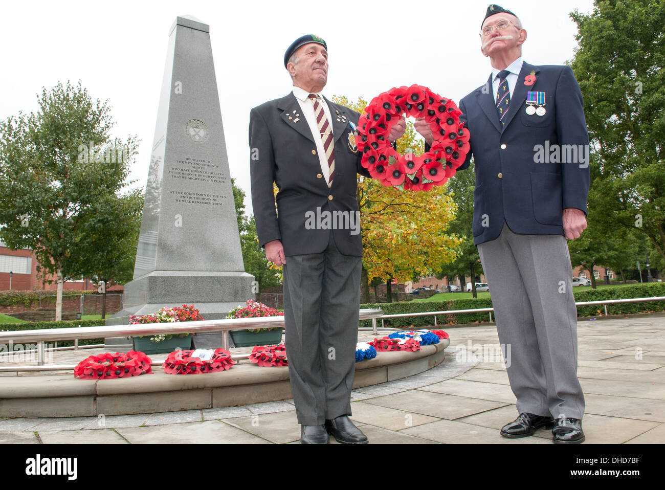 Two Second World War veterans stand to attention holding a wreath of Royal British Legion poppies beside a Dudley war memorial Stock Photo